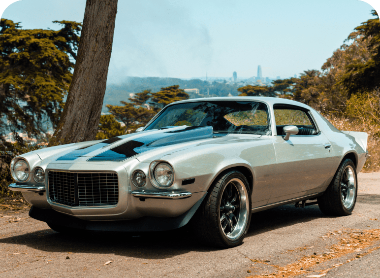 Classic silver muscle car with blue racing stripes parked outdoors.
