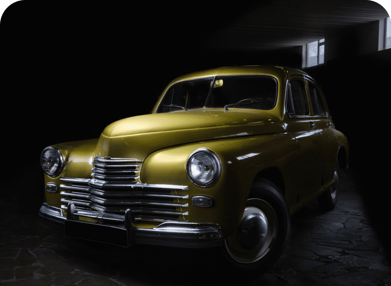 A vintage gold car in a dark garage with dramatic lighting.