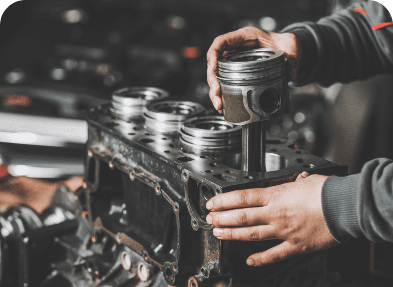Hands fitting a piston into an engine block during assembly.